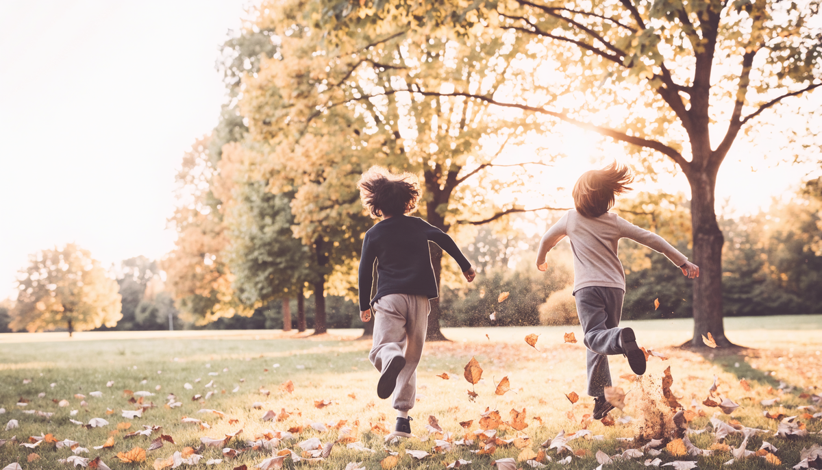 Zwei Kinder rennen von hinten gesehen durch Herbstlaub im Park, warmes Gegenlicht