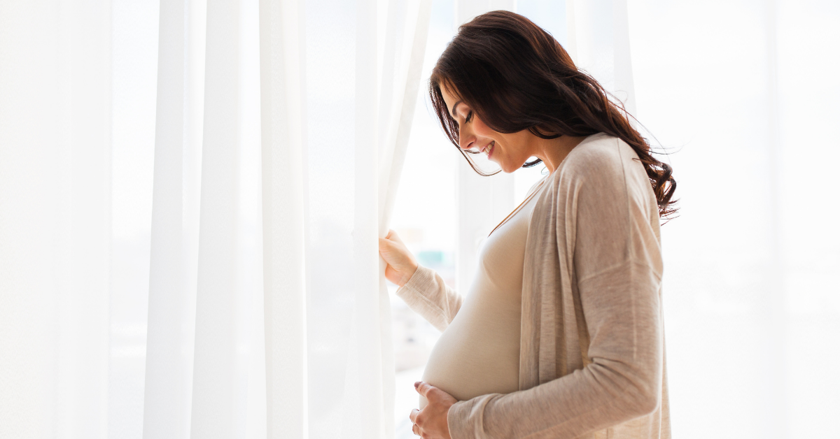 Schwangere Frau am Fenster – Folsäure Dosierung in Schwangerschaft und Kinderwunsch